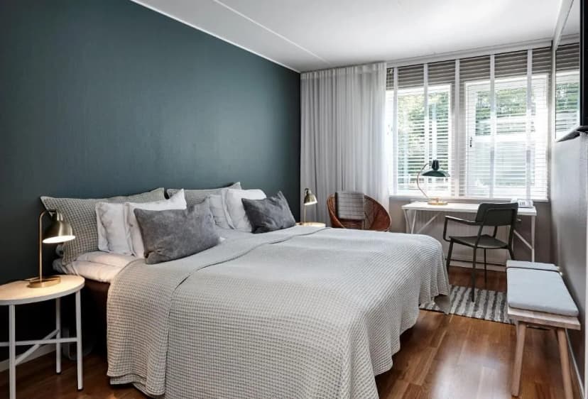 Bedroom at Aspenäs Herrgård with dark teal accent wall, white bedding, and wooden floor.