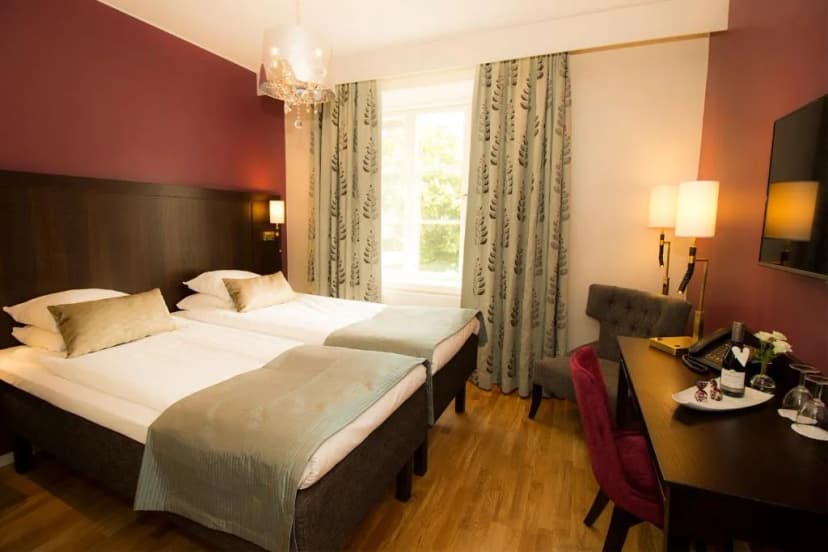 Twin beds in a hotel room with wood floors and burgundy accent wall at Grand Hotel Alingsås.