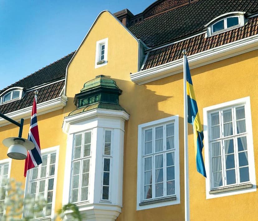 Yellow building facade of Grand Hotel Alingsås with Norwegian and Swedish flags flying.