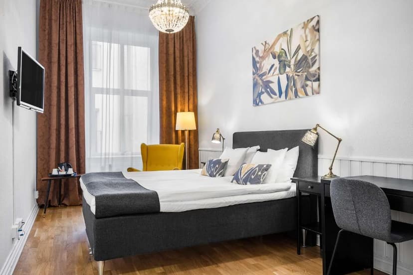 Hotel room with dark gray bed, yellow armchair, chandelier, and olive branch artwork.