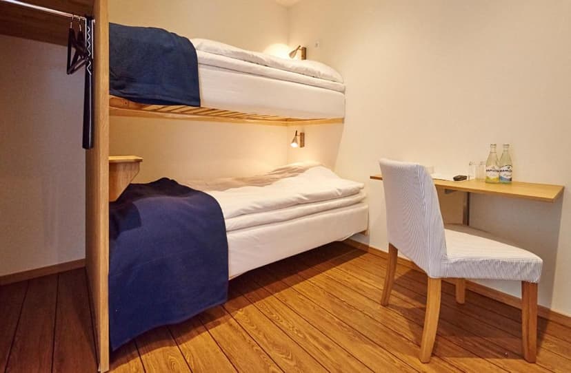 Bunk beds with white linens and blue throws in a simple hotel room with wooden floors.