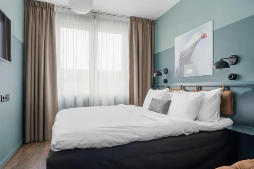 Bedroom with white bedding, blue-green walls, and a large window with sheer and brown curtains.
