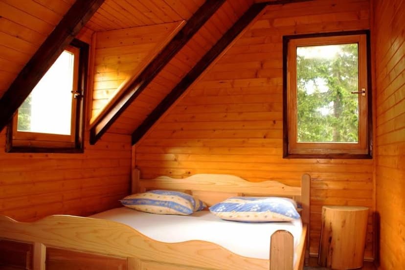Wooden cabin attic bedroom with pine walls, sloped ceiling, and view of green trees.
