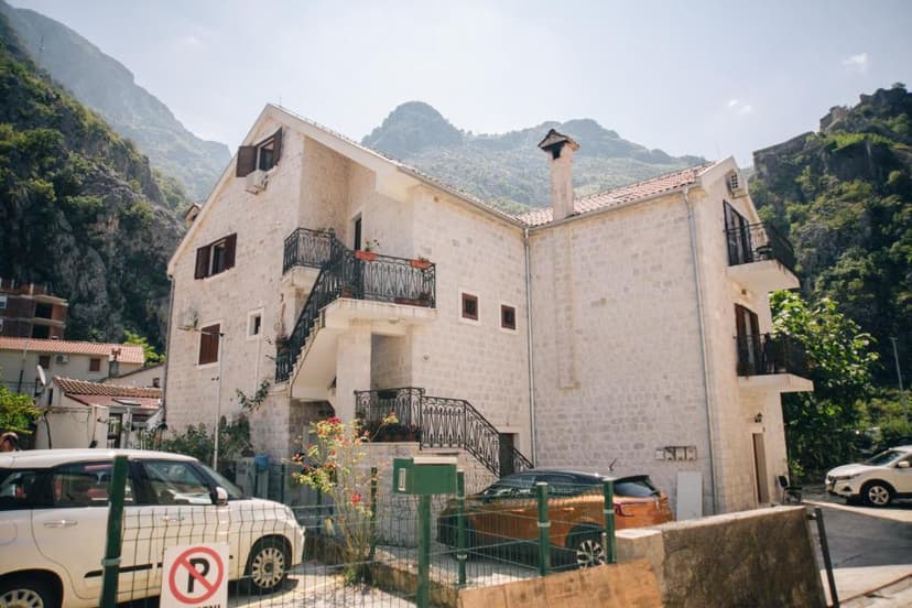 Stone building with outdoor stairs and balconies nestled against steep, green mountains.
