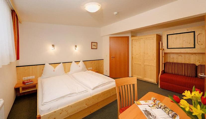Bright hotel room with pine wood furniture, double bed, red sofa, and flowers on table.