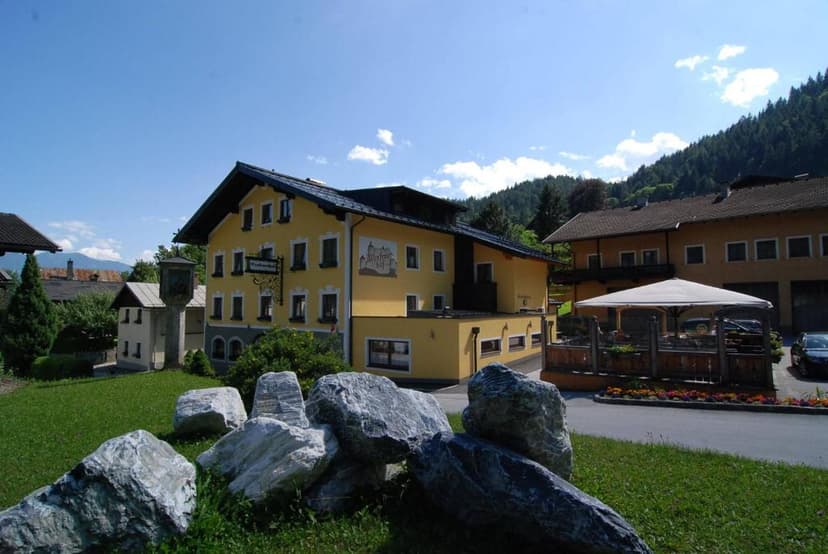 Yellow Werfenerhof building with outdoor seating area and large rocks in foreground, sunny day.