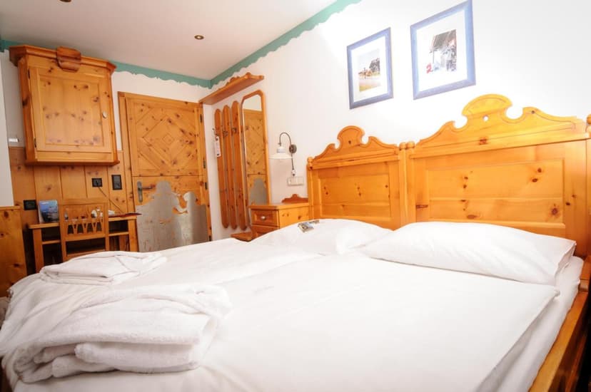 Double bed with white linens and robes in a room with light wood paneling and furniture at Berghotel Arthurhaus.