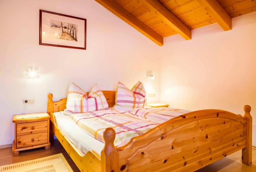 Wooden double bed with plaid bedding in room with exposed wood ceiling beams, Oberdachebenhof-Dienten.