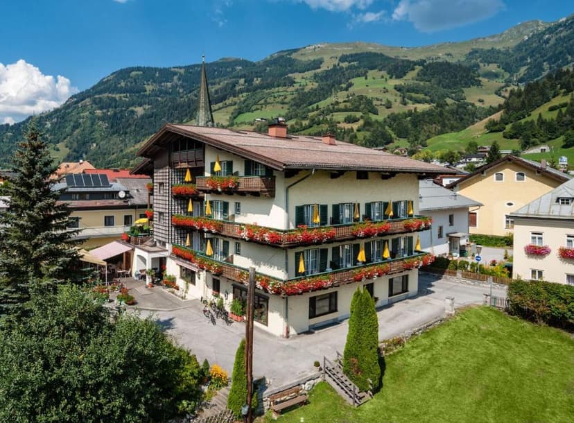Landhotel Steindlwirt building with flower boxes against green alpine mountains under blue sky.