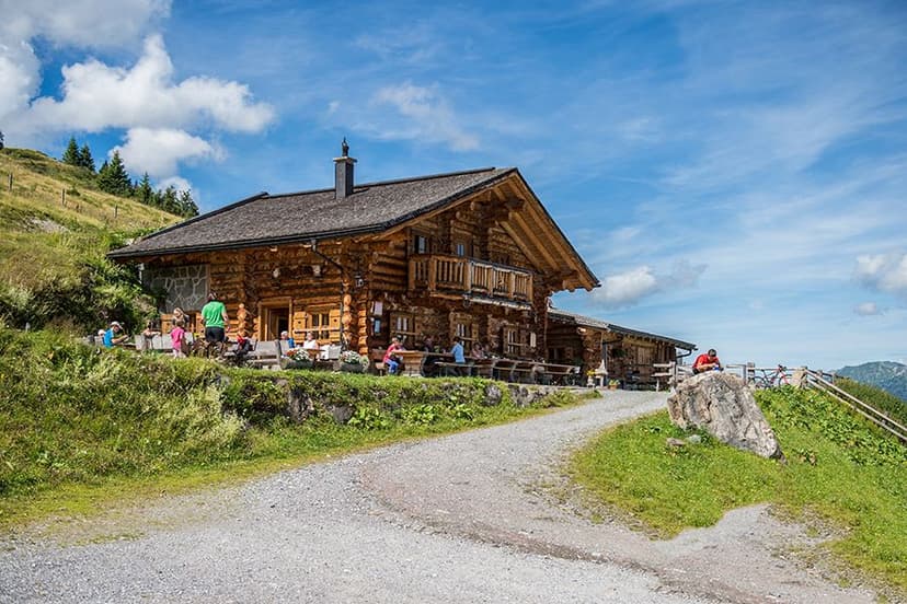 Log cabin mountain hut with outdoor seating on a sunny day, gravel path leading up