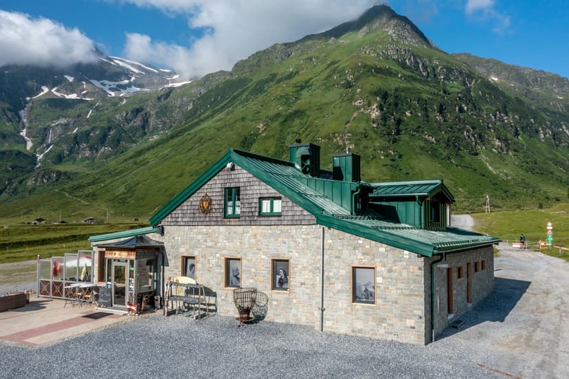 Stone building with green roof at base of lush green mountain with snow patches