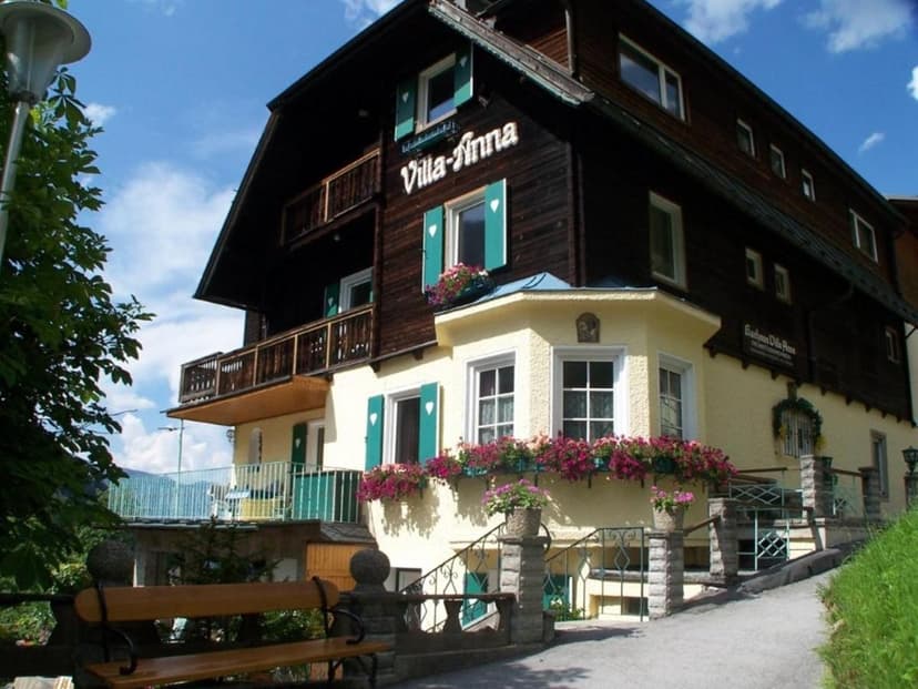 Pension Villa Anna with dark wood and yellow stucco, flower boxes, and bench.