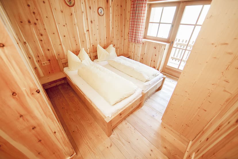 Twin beds in a room with light wood paneling and a window leading to a balcony at Loosbühelalm.