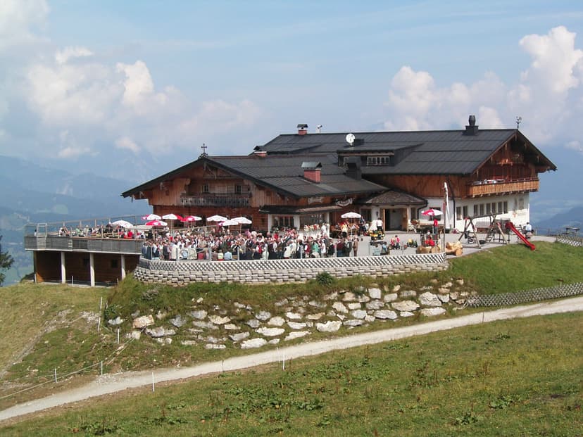 Buchau Hütte mountain restaurant with outdoor terrace and crowds, set against alpine backdrop.