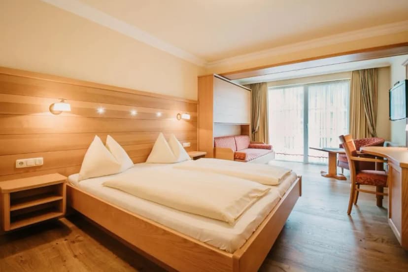 Hotel room with wooden furnishings, double bed, seating area, and balcony access at Hotel Guggenberger.