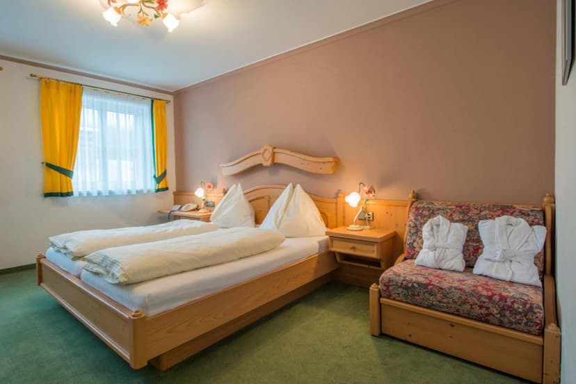 Hotel room with wooden bed, green carpet, and yellow curtains at Posthotel Radstadt