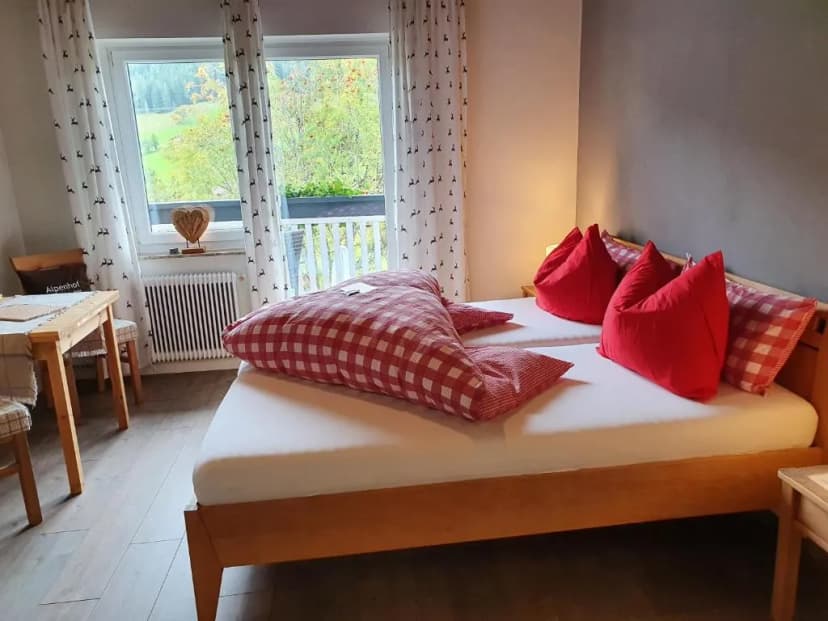 Boutique Hotel Alpenhof room with wooden bed, red pillows, and view of green hills.