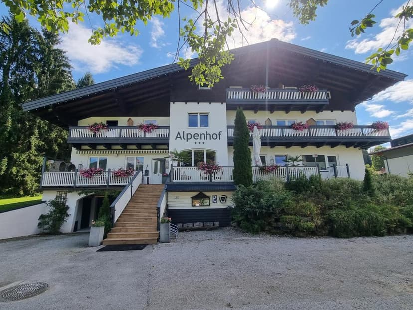 Boutique Hotel Alpenhof with white facade, dark wood trim, and flower boxes under sunny sky.