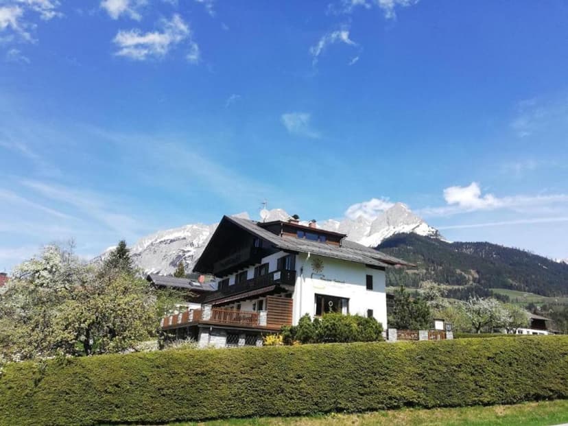 Alpine guesthouse with white facade below snow-capped mountains under blue sky