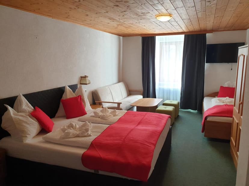 Hotel room with wooden ceiling, beds with red throws, and a bright window.