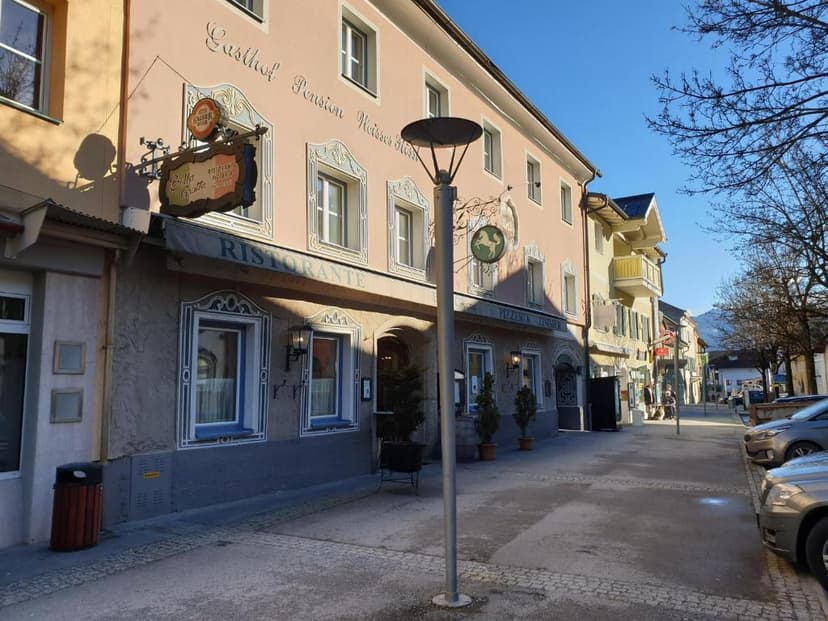 Gasthof Pension Weisses Rössl Ristorante on a sunny street with parked cars and distant mountains.