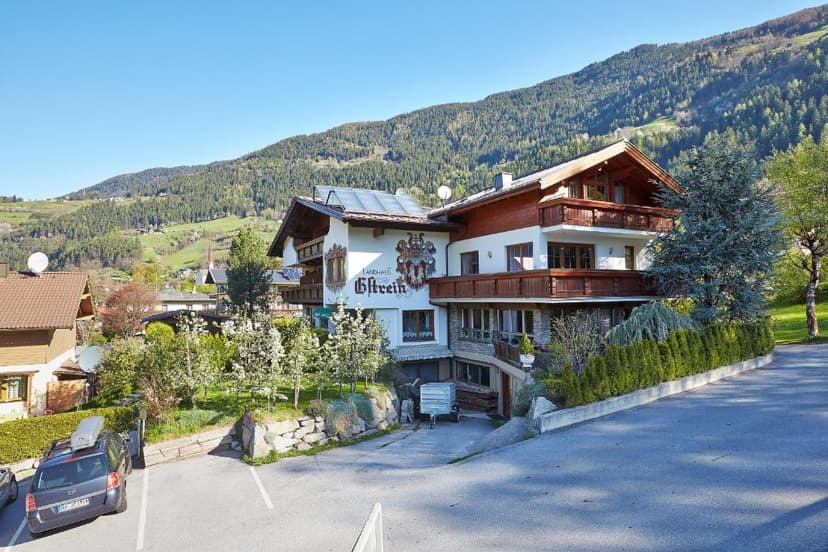 Landhaus Gstrein building with wooden balconies against a backdrop of green alpine mountains.