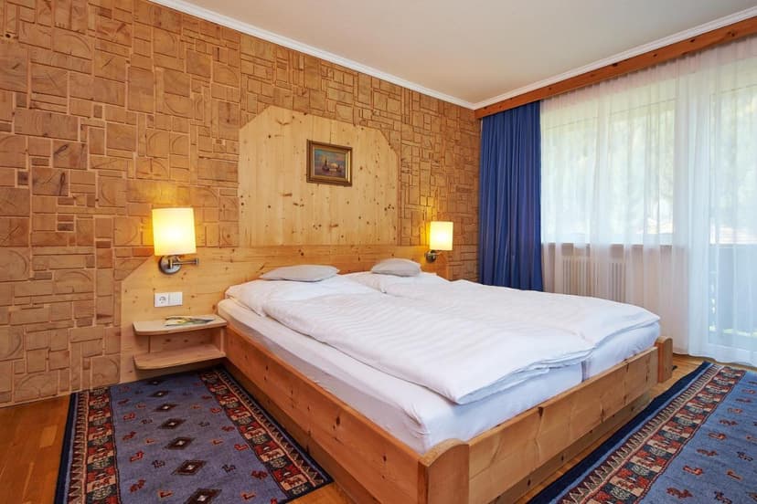 Double bed in rustic room with wood block walls and blue rug, APART-Landhaus-Gstrein