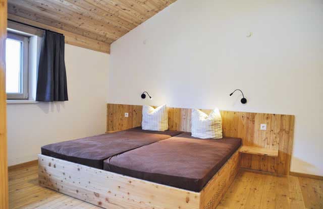 Twin beds with brown mattresses and white pillows in a room with wood ceiling and floor.