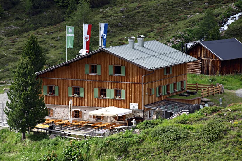 Schweinfurter Hütte wooden mountain lodge with outdoor seating and flags on grassy slope.