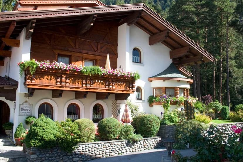 Gästehaus Sissy with wooden balcony and flower boxes, set against a dense forest backdrop.
