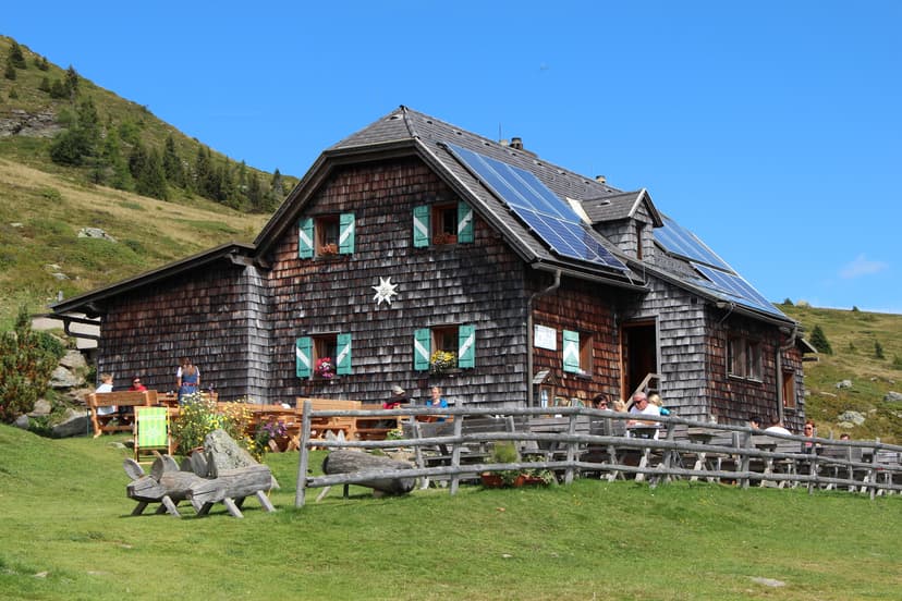 Millstätter Hütte alpine hut with solar panels and outdoor seating on grassy mountain slope.