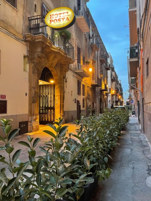 Hotel Posta sign above entrance on narrow European street lined with potted plants