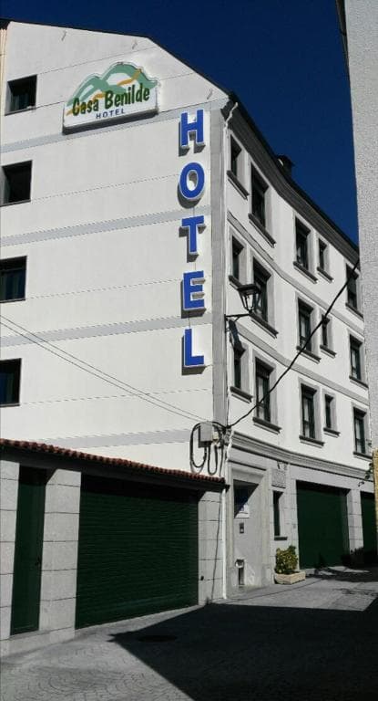 Hotel Casa Benilde exterior wall with vertical blue "HOTEL" sign under clear blue sky.