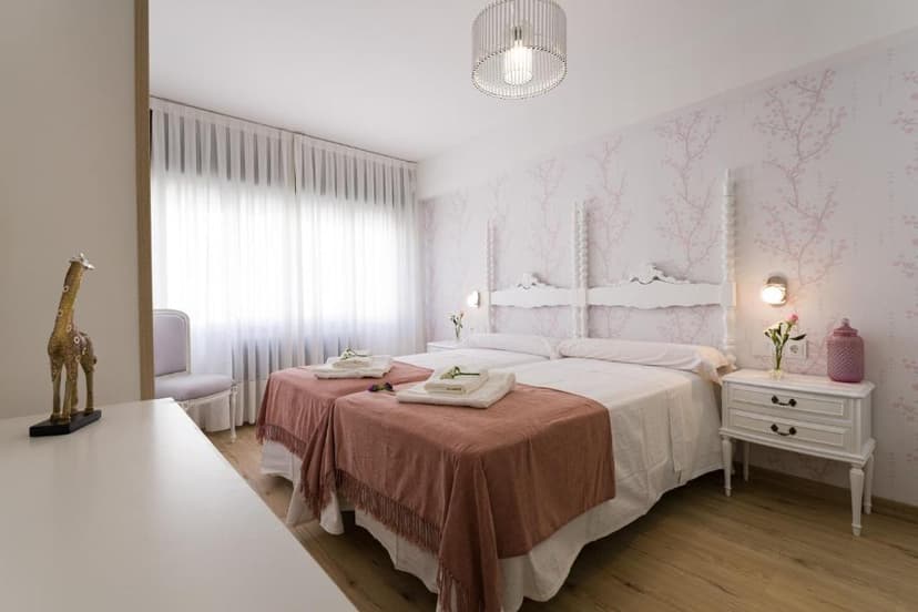 Twin beds with white linens and pink throws, cherry blossom wallpaper, and wood floor
