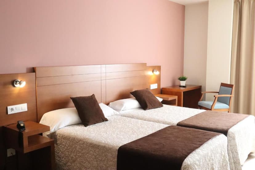 Twin hotel room with brown bedding, pink wall, and light wood furniture in Hotel Arzua.