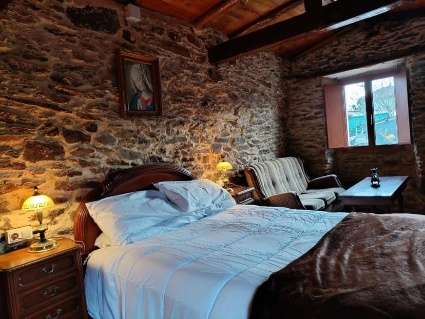 Cozy bedroom with stone walls, wooden ceiling, and a large bed at Granja del Peregrino.