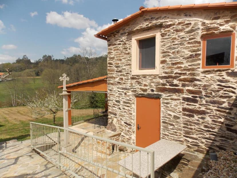Stone building with orange door and cross monument overlooking green fields near Granja del Peregrino.