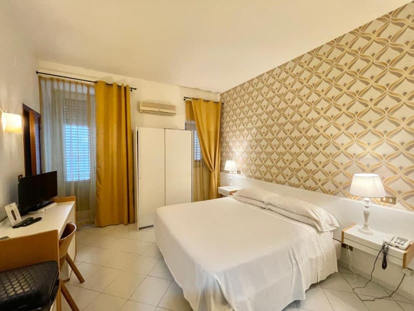 Hotel room with white bedding, patterned wallpaper, yellow curtains, and white tile floor