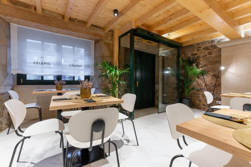Dining area in Hostal Celenis with stone walls, wood beams, and white modern chairs.
