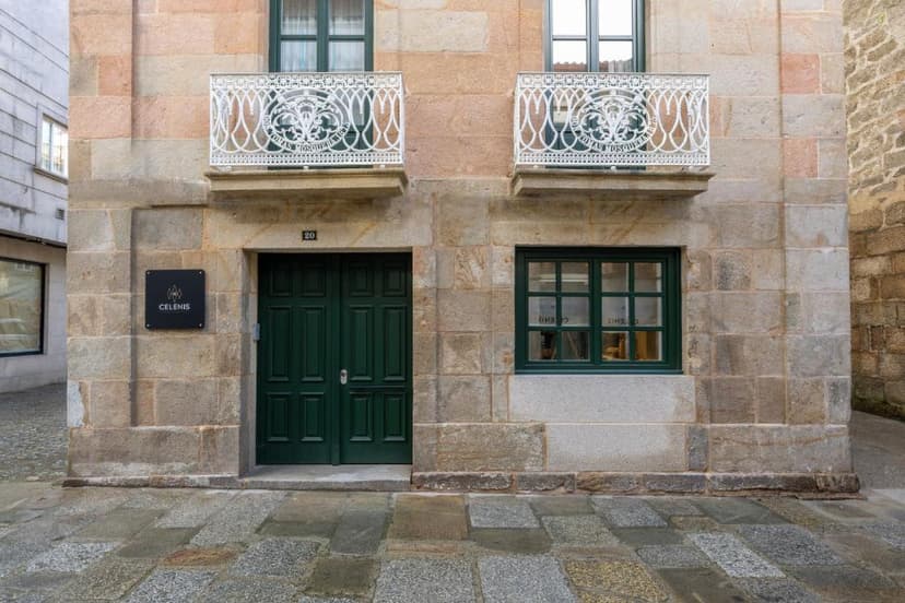 Stone building facade with green door, white balconies, and "CELENIS" sign on wet cobblestones