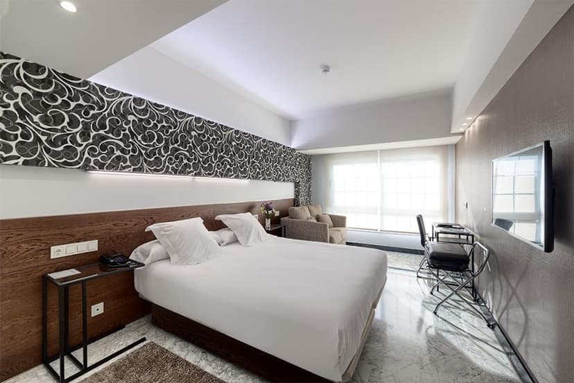 Modern hotel bedroom with white bedding, patterned accent wall, and marble floor, Hotel Avenida.