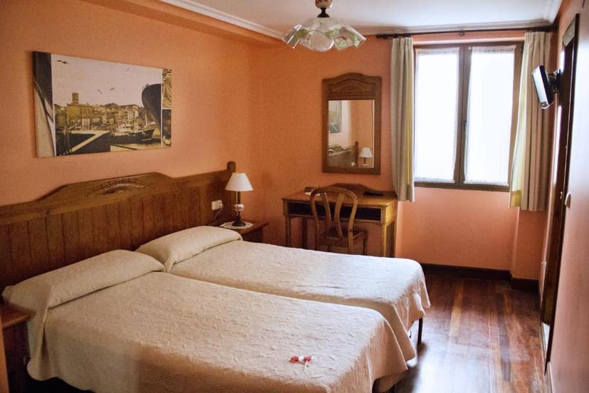 Twin beds in a hotel room with peach walls, wooden headboard, desk, and bright window.