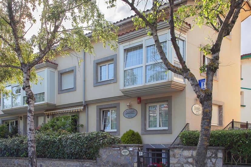 Zumardi Pension building facade with bay windows, surrounded by leafy trees and green hedges.