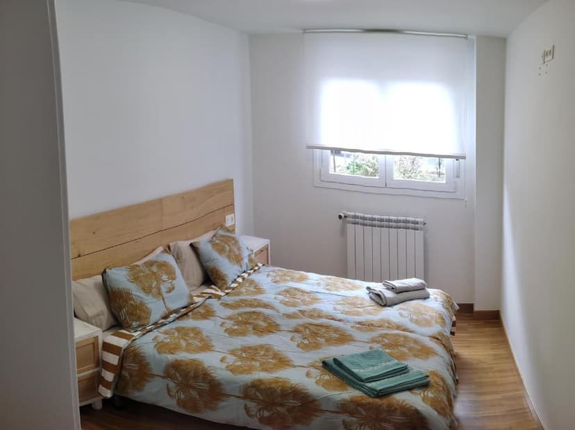 Bedroom with wooden headboard, palm print duvet, and white walls near a window with a radiator.