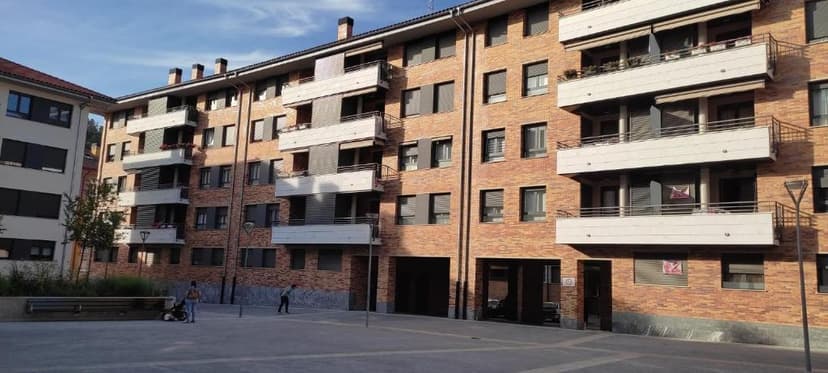 Brick apartment building with balconies and a paved plaza with people in the foreground.