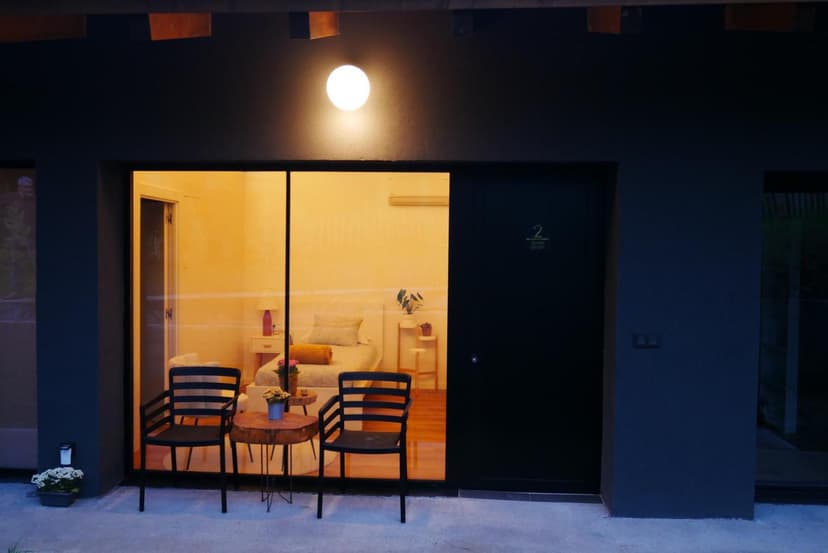 Outdoor patio with two chairs and a wooden table in front of a brightly lit hotel room at night.