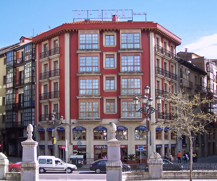 Red hotel building with many windows on a city street corner in Bilbao.