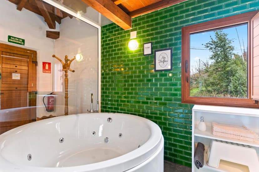 Round jacuzzi tub next to green subway tile wall and window showing trees outside