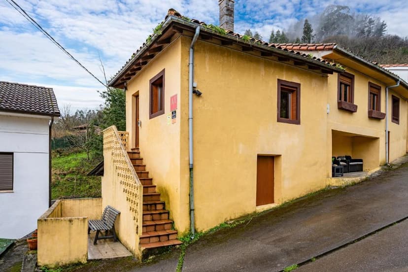 Yellow stucco house with exterior stairs, bench, and mountain backdrop under cloudy sky.