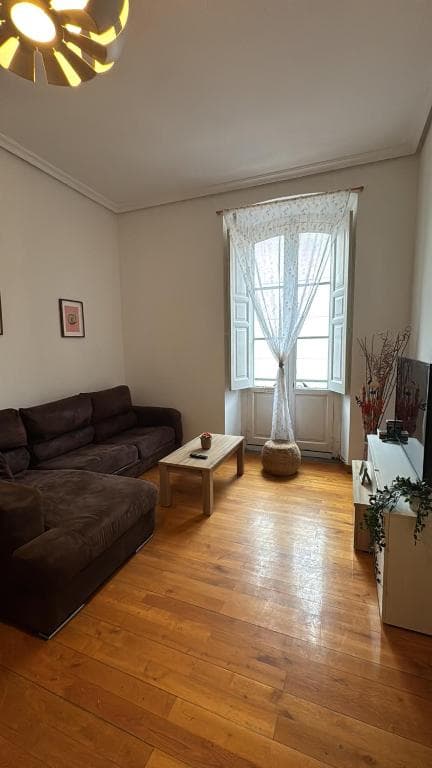 Living room with dark sectional sofa, wooden coffee table, and window with sheer curtain